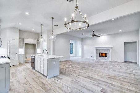 Kitchen featuring hanging light fixtures, a fireplace, ceiling fan with notable chandelier, sink, and an island with sink