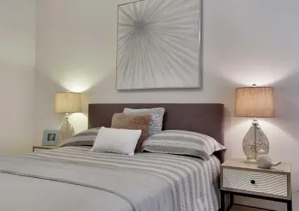 Bed with gray linens, side tables with lamps and a decorative wall hanging.