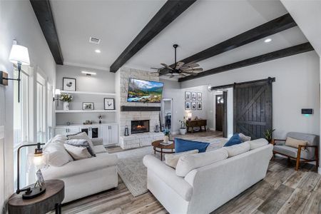 Living room with beam ceiling, a stone fireplace, a barn door, and light wood-type flooring