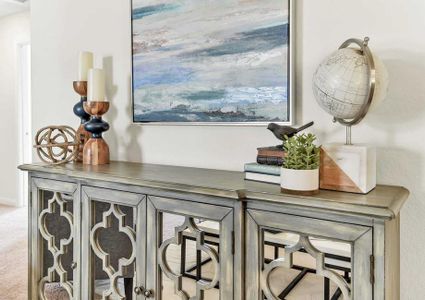 Model home with a seascape painting on the wall plus a globe, books, and candles sitting on a decorative wooden credenza with mirrored doors