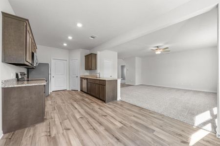 Kitchen featuring appliances with stainless steel finishes, sink, ceiling fan, light stone countertops, and light hardwood / wood-style flooring