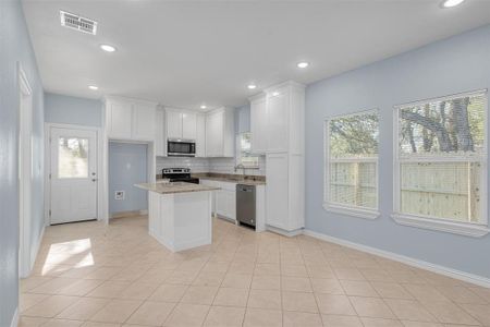 Kitchen with a wealth of natural light, a kitchen island, light stone counters, and appliances with stainless steel finishes