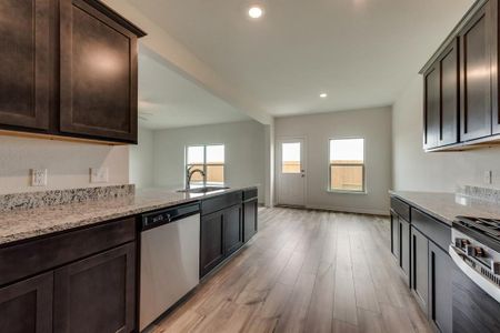 Kitchen with dark brown cabinets, light wood-type flooring, sink, light stone counters, and appliances with stainless steel finishes