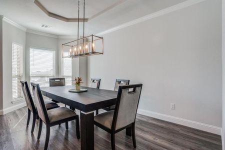 Dining space featuring dark wood-type flooring, a raised ceiling, ornamental molding, and an inviting chandelier