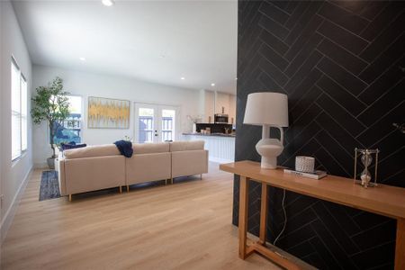 Living room with light hardwood / wood-style floors, tile walls, and french doors