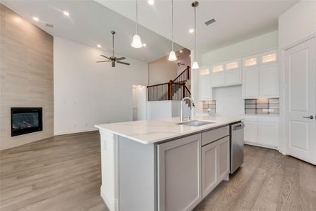 Kitchen featuring light hardwood / wood-style flooring, light stone countertops, a center island with sink, a tile fireplace, and sink