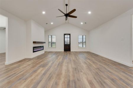 Unfurnished living room featuring ceiling fan, lofted ceiling, and light hardwood / wood-style flooring