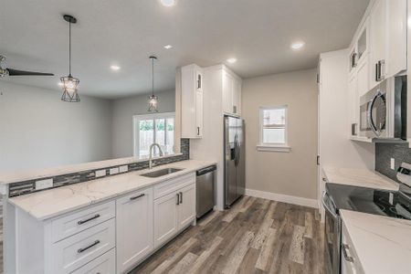 Kitchen featuring appliances with stainless steel finishes, white cabinets, backsplash, pendant lighting, and sink