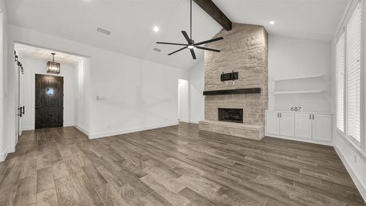 Unfurnished living room featuring ceiling fan, a stone fireplace, high vaulted ceiling, hardwood / wood-style floors, and beamed ceiling