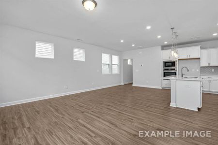 Kitchen featuring appliances with stainless steel finishes, dark wood-type flooring, sink, pendant lighting, and a center island with sink