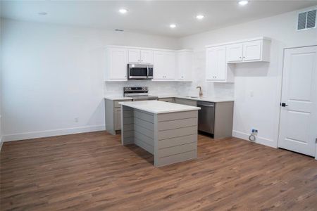 Kitchen with dark hardwood / wood-style flooring, stainless steel appliances, sink, white cabinetry, and a kitchen island