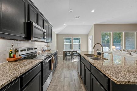 Kitchen with tasteful backsplash, appliances with stainless steel finishes, sink, light hardwood / wood-style floors, and lofted ceiling