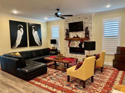 Living room featuring ceiling fan, ornamental molding, a stone fireplace, and wood-type flooring