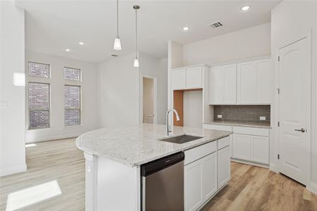 Kitchen with stainless steel dishwasher, white cabinets, sink, and an island with sink