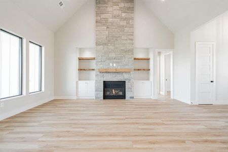 Example of living room featuring high vaulted ceiling, built in features, light hardwood / wood-style floors, and a stone fireplace