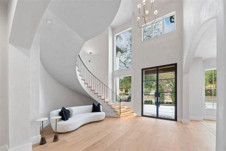 You're looking at a modern entryway featuring elegant arched doorways, a sweeping staircase with a stylish black handrail, and large windows that bathe the space in natural light. The warm wood flooring and neutral tones create a welcoming atmosphere.