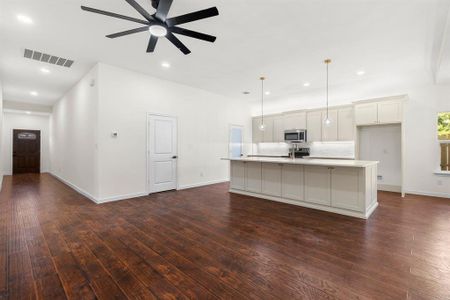 Kitchen with appliances with stainless steel finishes, decorative light fixtures, dark hardwood / wood-style floors, an island with sink, and ceiling fan