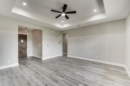 Unfurnished room with light hardwood / wood-style floors, a raised ceiling, and ceiling fan