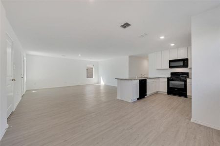 Kitchen with light wood-type flooring, white cabinetry, sink, black appliances, and kitchen peninsula