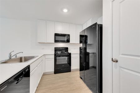 Kitchen with sink, white cabinets, black appliances, and light hardwood / wood-style flooring