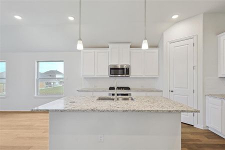 Kitchen featuring hanging light fixtures, light hardwood / wood-style floors, light stone counters, an island with sink, and white cabinets