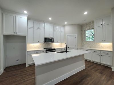 Kitchen with dark wood-type flooring, a center island with sink, appliances with stainless steel finishes, and sink