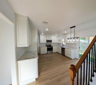 Kitchen featuring backsplash, hanging light fixtures, stainless steel appliances, white cabinets, and light stone counters