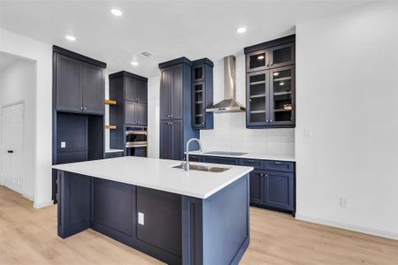 Kitchen with light wood-type flooring, a kitchen island with sink, wall chimney exhaust hood, and sink