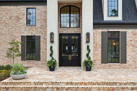 A grand brick staircase leads to the striking double doors, framed by an arched transom and flanked by elegant gas lanterns. Thoughtfully placed shutters, lush greenery, and timeless architectural details create an inviting entry that perfectly blends classic charm with modern sophistication.