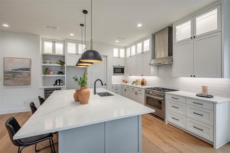 Kitchen featuring light hardwood / wood-style floors, high end stainless steel range oven, built in microwave, wall chimney exhaust hood, and a kitchen island with sink