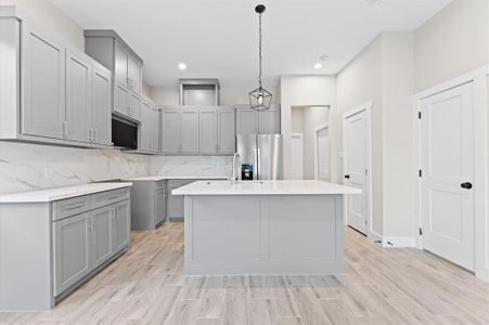 This modern kitchen features sleek gray cabinets, a large central island with a quartz countertop, stainless steel appliances, and stylish light fixtures. The space is bright and open, with wood-look flooring and ample storage.