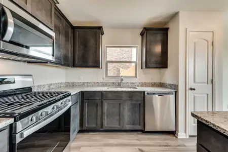 Kitchen featuring light stone countertops, light hardwood / wood-style floors, dark brown cabinetry, sink, and appliances with stainless steel finishes