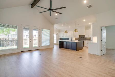 Kitchen featuring a center island with sink, decorative light fixtures, light wood-type flooring, high vaulted ceiling, and white cabinets