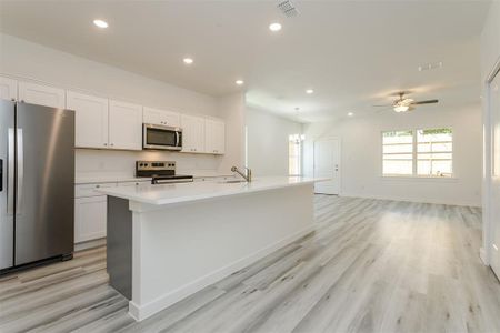 Kitchen with stainless steel appliances, a center island with sink, light hardwood / wood-style flooring, and white cabinets