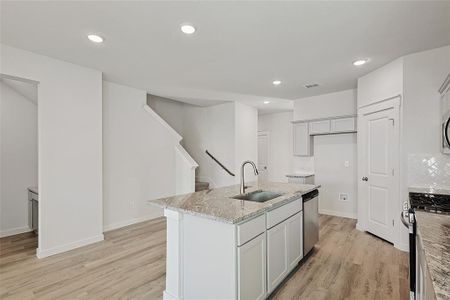 Kitchen with light stone countertops, sink, appliances with stainless steel finishes, light hardwood / wood-style flooring, and a kitchen island with sink