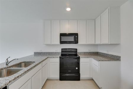 Kitchen with black appliances, white cabinets, sink, light stone countertops, and light tile patterned flooring