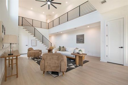 Living room featuring ceiling fan, a towering ceiling, and light wood-type flooring