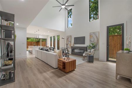 Living room with a high ceiling, ceiling fan with notable chandelier, and light wood-type flooring