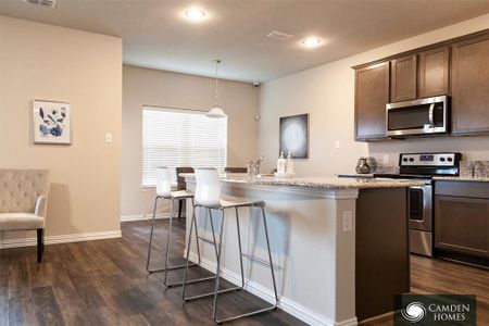 Kitchen with dark wood-type flooring, hanging light fixtures, an island with sink, light stone counters, and stainless steel appliances