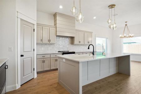 Kitchen with backsplash, light hardwood / wood-style flooring, an island with sink, and pendant lighting