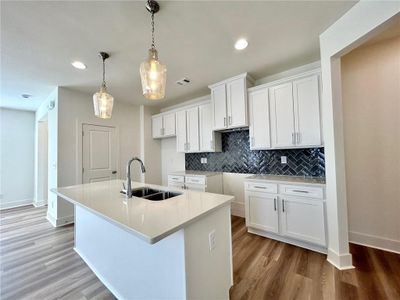 Kitchen featuring a kitchen island with sink, pendant lighting, light hardwood / wood-style flooring, and white cabinets