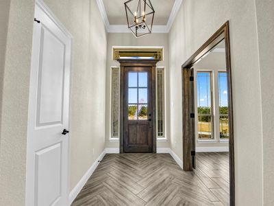 Foyer entrance with a notable chandelier, ornamental molding, and light parquet floors