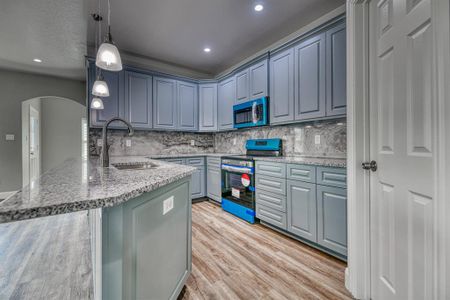 Kitchen with light stone countertops, tasteful backsplash, stainless steel appliances, decorative light fixtures, and light wood-type flooring