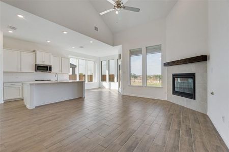 Kitchen featuring high vaulted ceiling, light hardwood / wood-style floors, white cabinetry, and a tiled fireplace