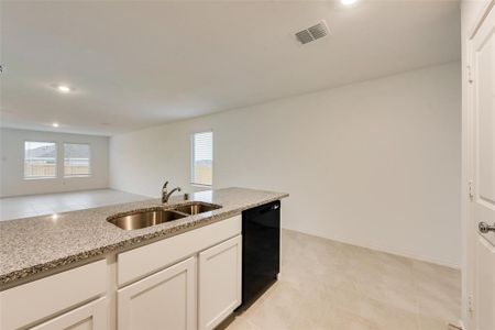 Kitchen with black dishwasher, sink, light stone counters, and white cabinetry