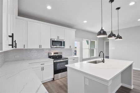 Kitchen with a center island with sink, sink, appliances with stainless steel finishes, decorative light fixtures, and white cabinetry