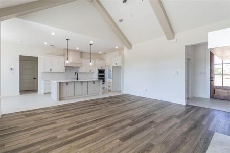 Unfurnished living room featuring hardwood / wood-style flooring, beam ceiling, sink, and high vaulted ceiling