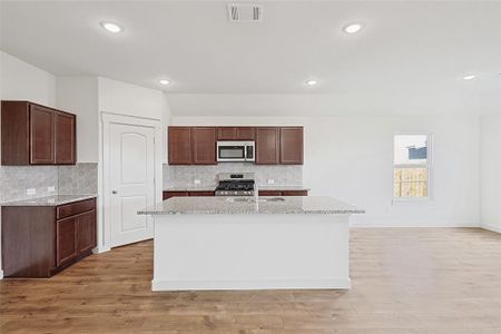 Kitchen with decorative backsplash, appliances with stainless steel finishes, a center island with sink, and light hardwood / wood-style flooring