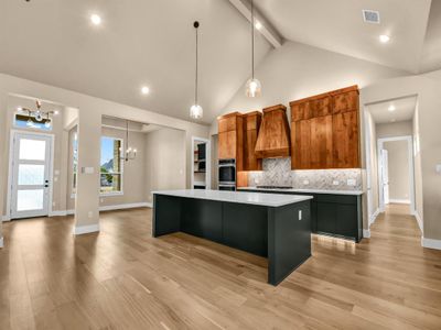 Kitchen featuring a large island, tasteful backsplash, high vaulted ceiling, a notable chandelier, and premium range hood