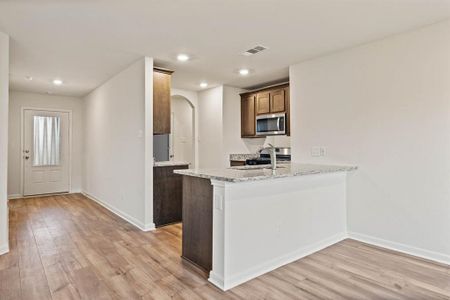 Kitchen featuring stainless steel microwave, visible vents, baseboards, light wood-type flooring, and arched walkways